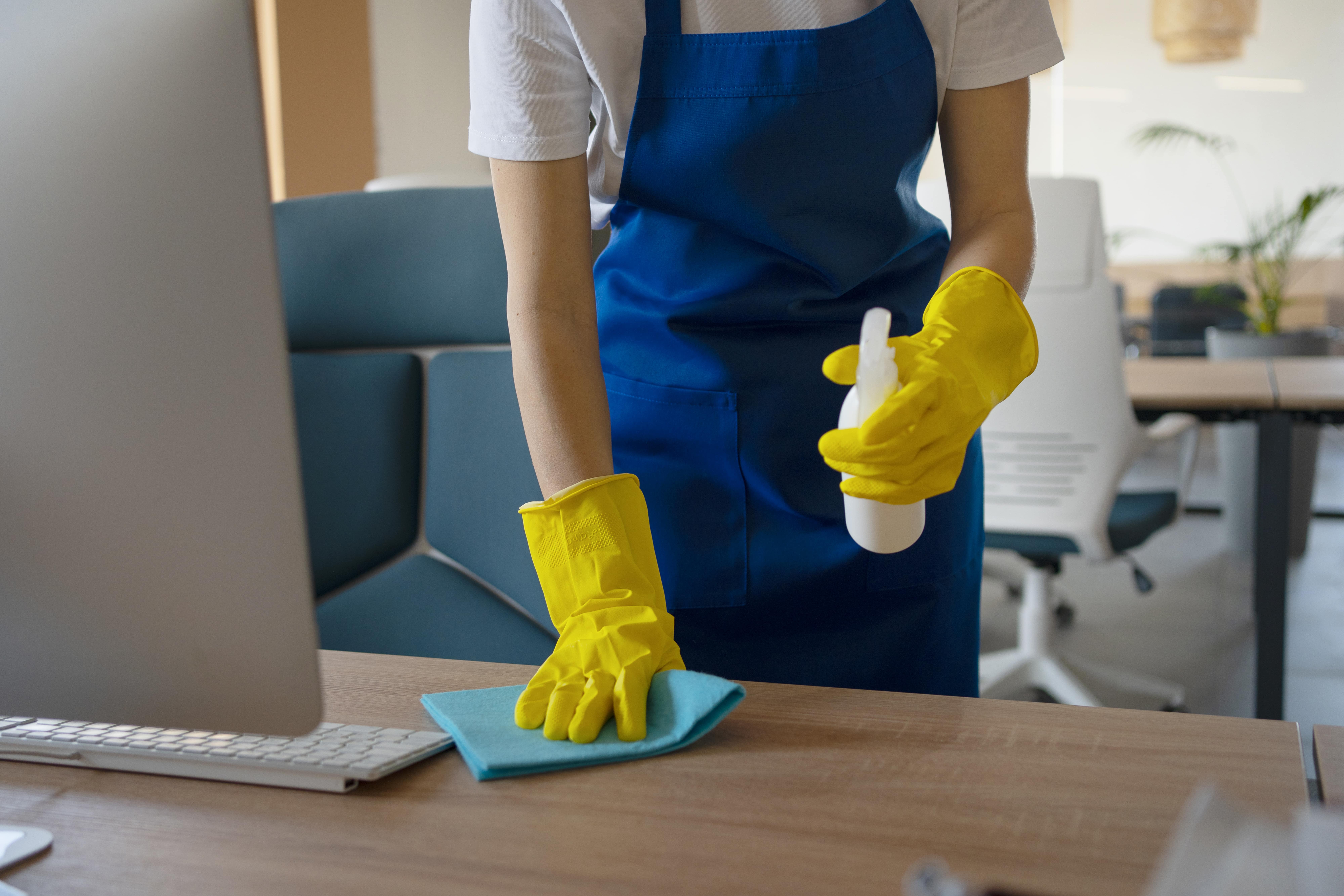 Schoonmaker desinfecteert en reinigt bureau in kantoorruimte met microvezeldoek – Cleaning Service Eindhoven